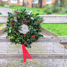 Load image into Gallery viewer, Holly and ivy Christmas wreath with a red ribbon on a gate